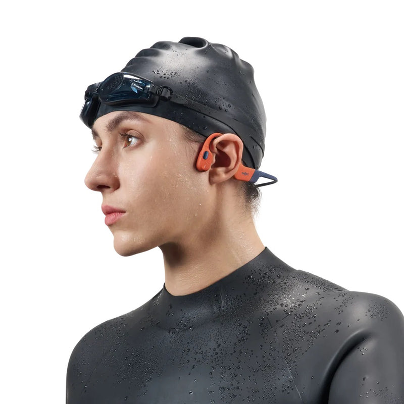 Person wearing a black swim cap and wet suit with OpenSwim Pro headphones on a white background